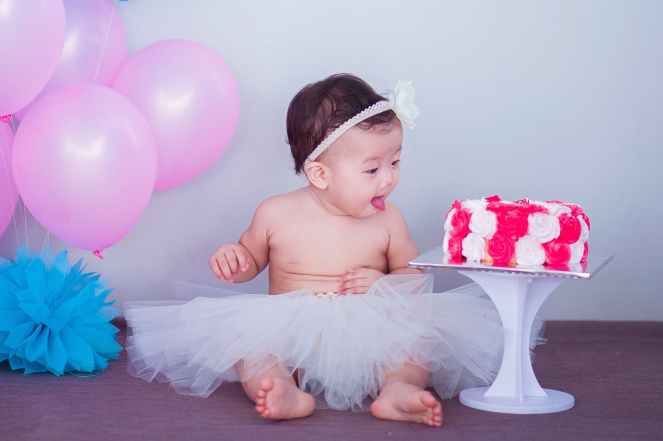 baby in white tutu skirt beside cake